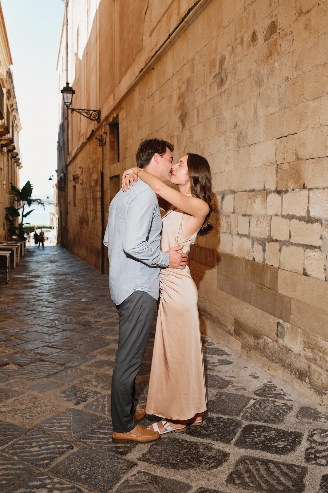Couple kissing in a narrow street of Ortigia, the light of the sea at the end