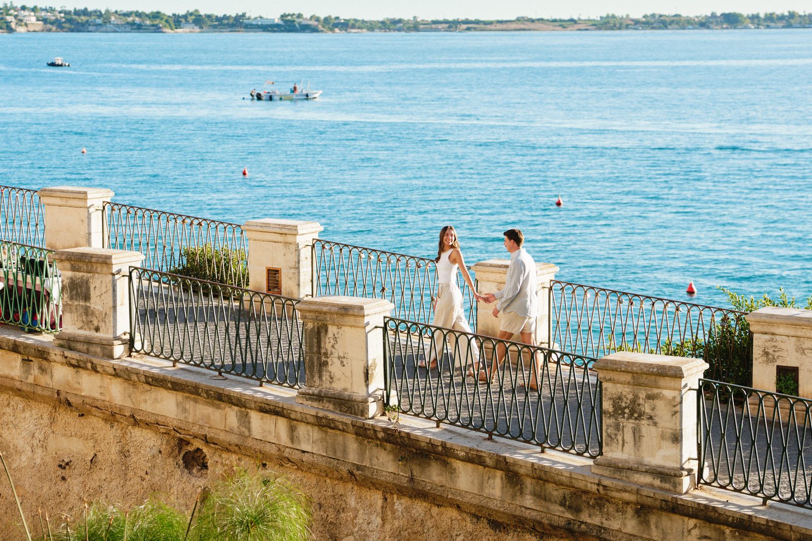 Couple photoshoot in Ortigia, Syracuse: Sophia and Will by the railing of Lungomare Alfeo, the sea all around