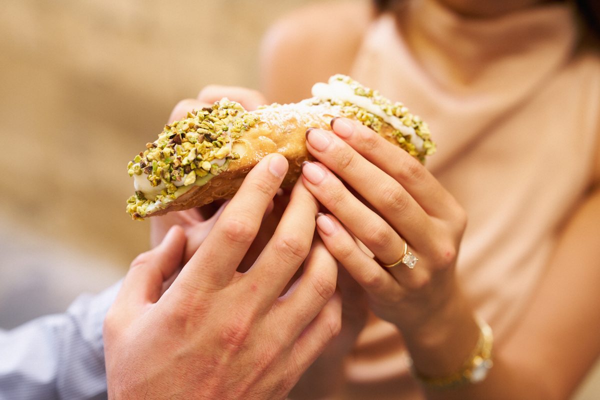 A pistachio cannolo in her hands during the couple photoshoot in Ortigia