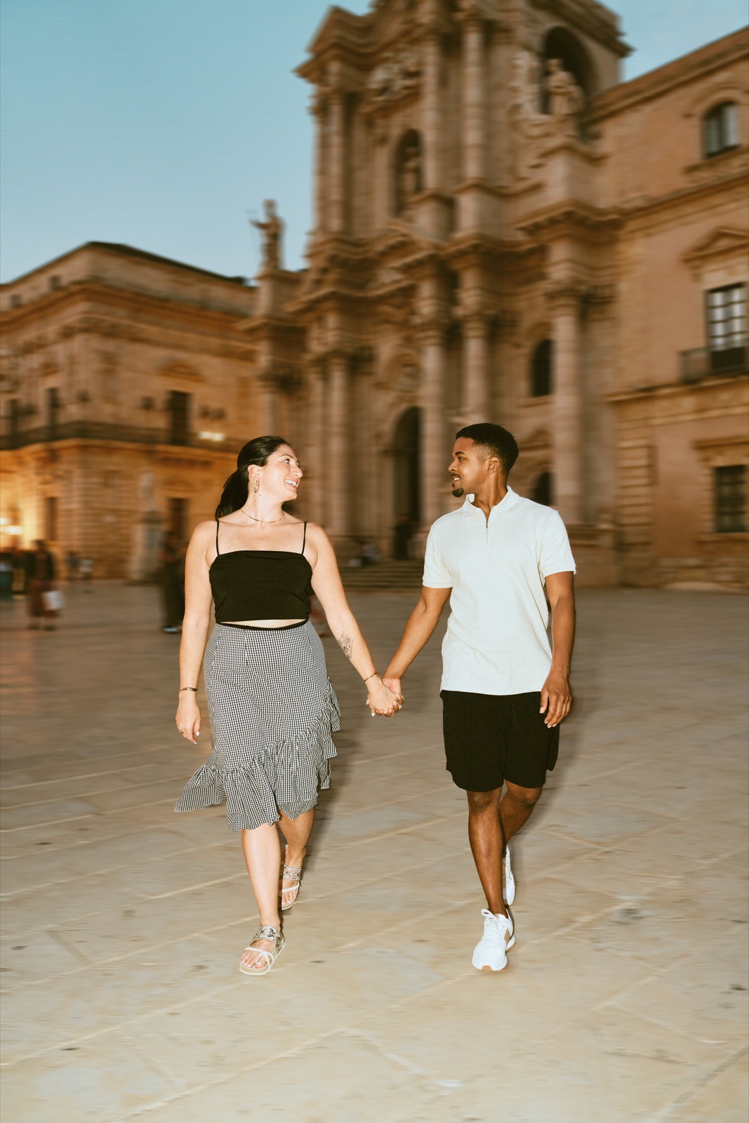 Engaged couple walking hand in hand across Piazza Duomo, Syracuse
