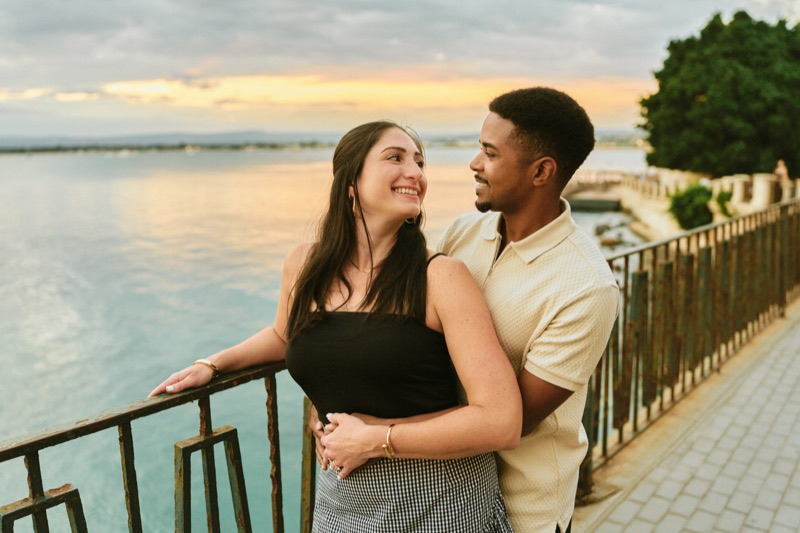 Engaged couple at sunset by the railing of Lungomare Alfeo, Ortigia